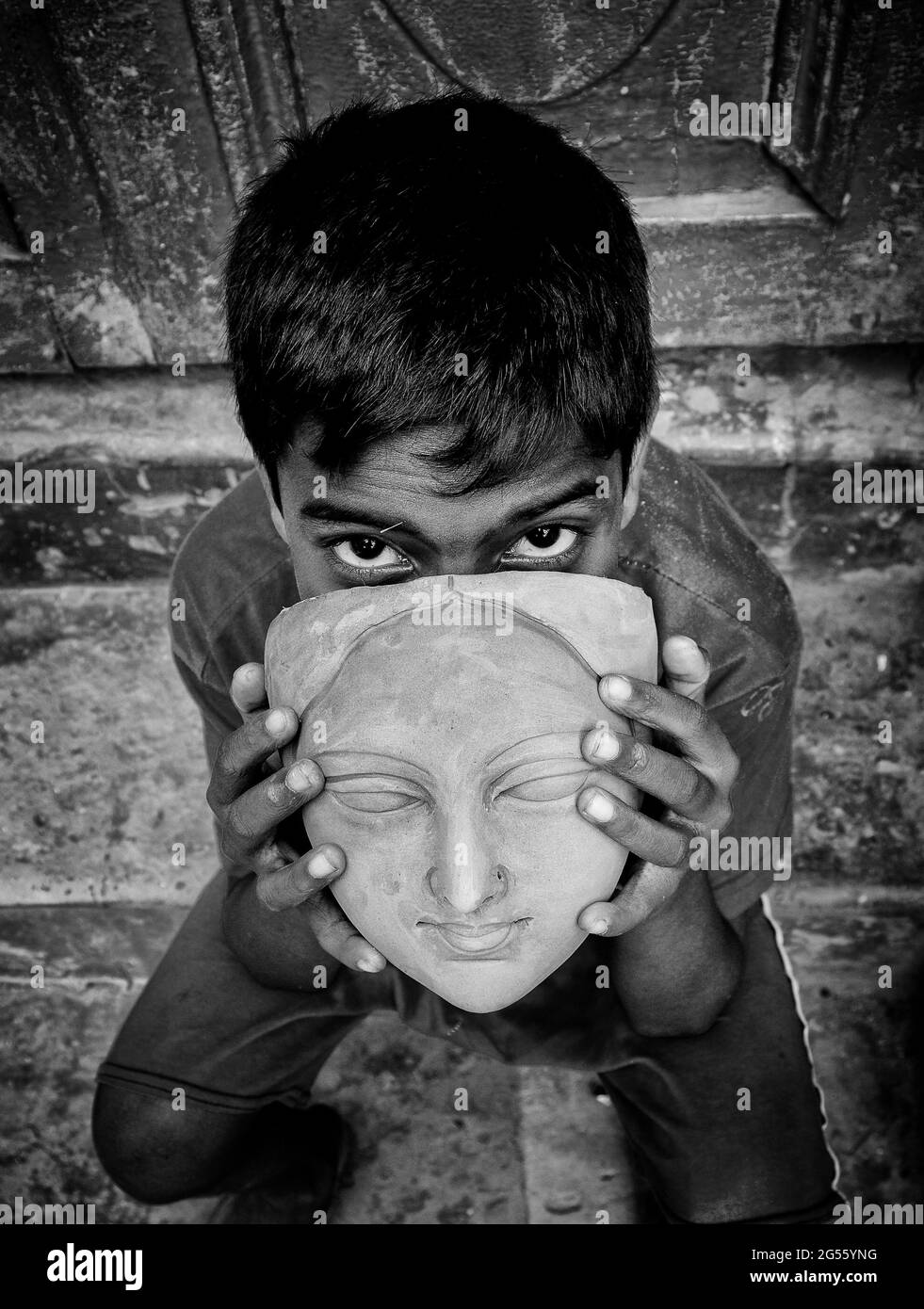 Ein kleines Kind posiert für die Kamera mit einem unvollendeten Kopf eines Durga-Idols an einem Töpferzentrum in Kalkutta, Indien. Stockfoto