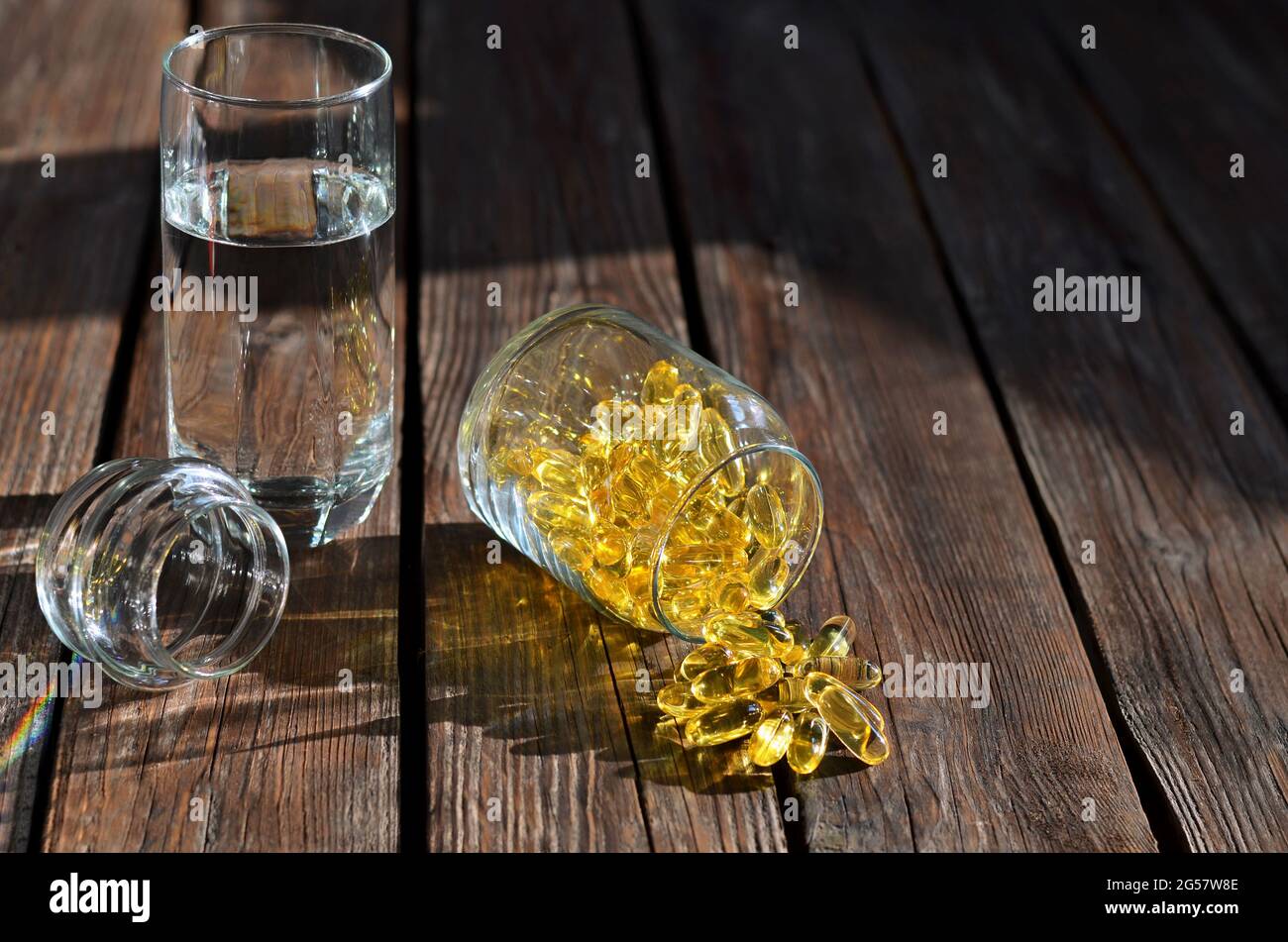 Nahrungsergänzungsmittel in gelben Gelatinekapseln in einem Glas neben einem Glas Wasser auf einem Holztisch. Vitamine für Gesundheit und Langlebigkeit. Stockfoto