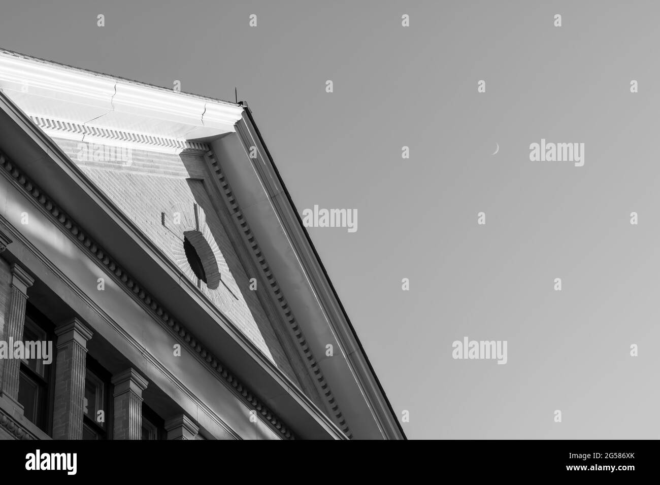 Schwarz-weiß eines Giebeldachs mit einem oculus-Fenster an der Außenfassade. Splitter Mond am Himmel. Platz für Text. Stockfoto