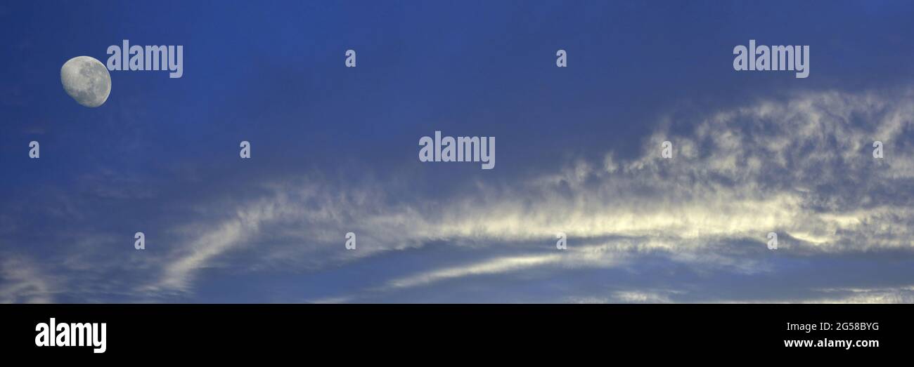 Eine lebhafte atmosphärische Wolkenlandschaft mit weißen Altostratus-Wolken und einem abnehmenden Mond in einem mittelblauen Himmel. Schönheit in der Natur. Neu Stockfoto