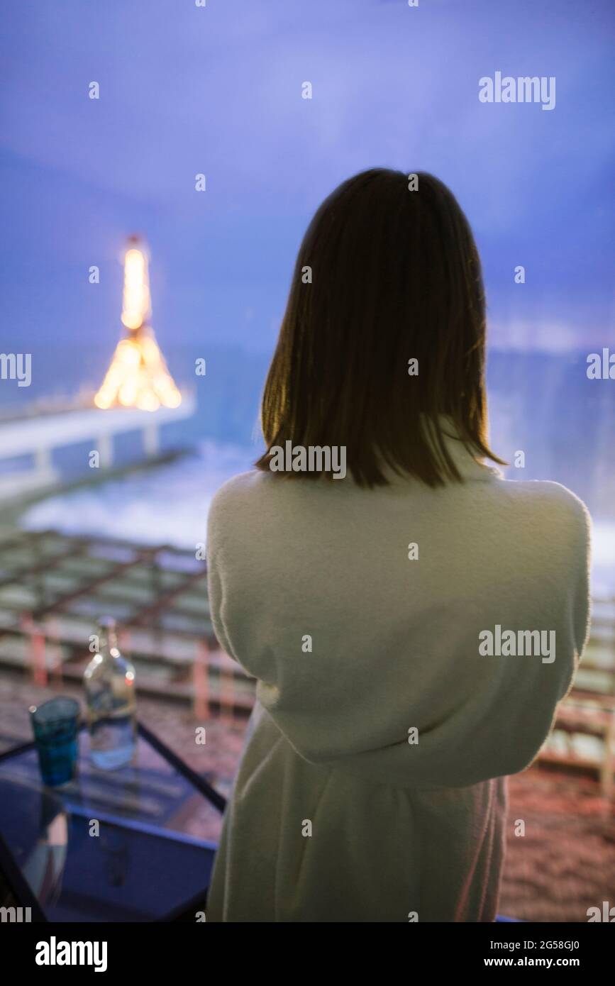Rückansicht einer Frau im Bademantel im Hotel mit Blick auf das Meer in der Nacht Stockfoto