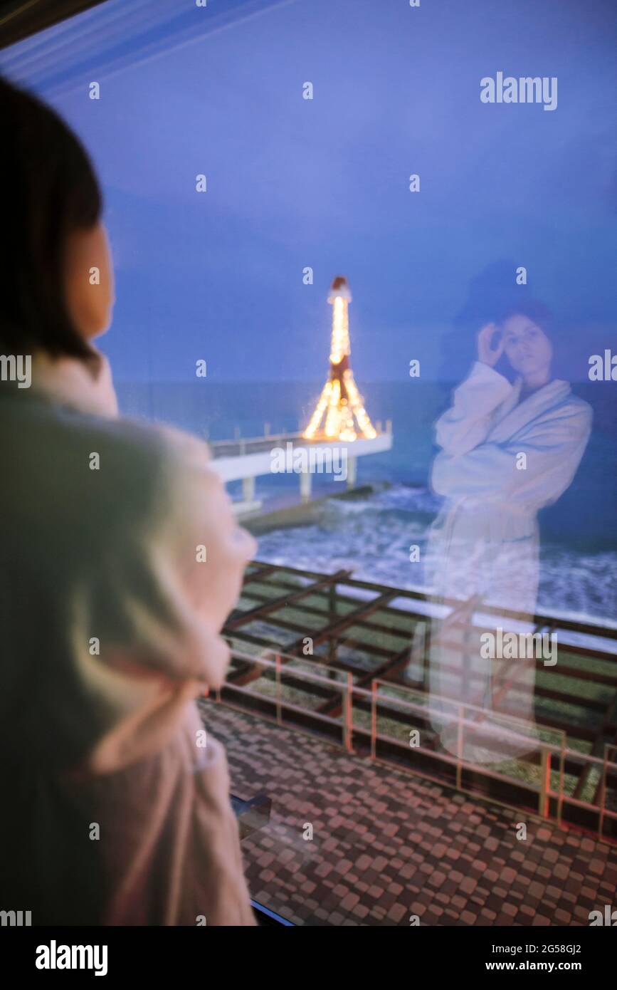 Rückansicht einer Frau im Bademantel im Hotel mit Blick auf das Meer in der Nacht Stockfoto