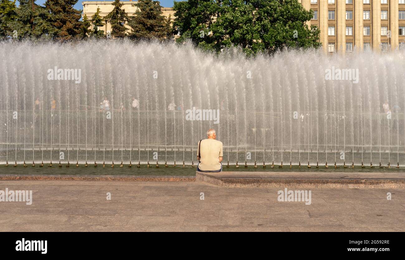 Ein Mann, der an einem heißen Sommertag am besprühenden Brunnen sitzt, Blick nach hinten, Moskovskaya-Platz, St. petersburg, Russland Stockfoto