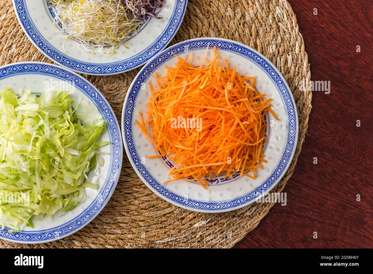 Rohe Julienne in Scheiben geschnittene Karotten, Luzerne und Eisbergsalat auf einem Holztisch Stockfoto
