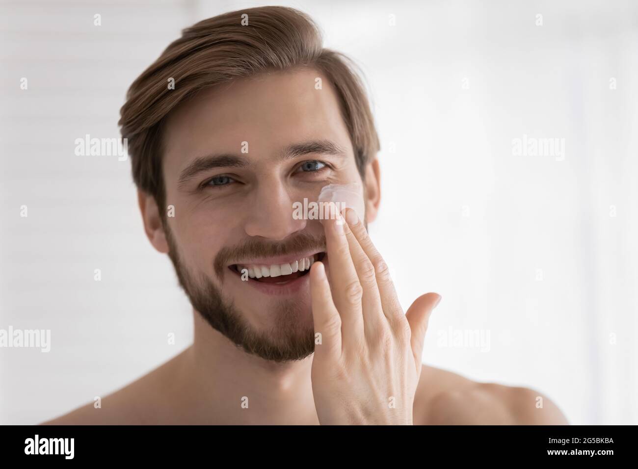 Kopfschuss von jungen attraktiven Kerl Anwendung Feuchtigkeitscreme Stockfoto