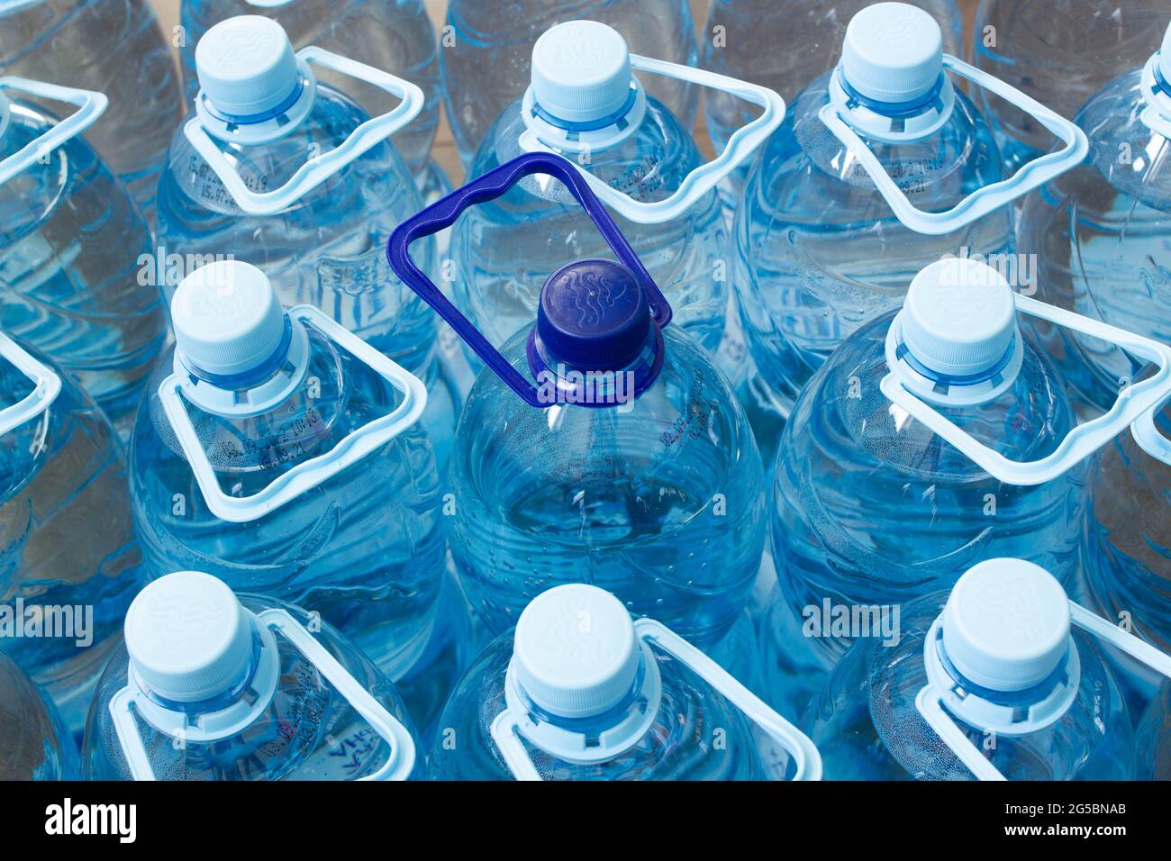 Viele blaue Plastikflaschen mit blauen Kappen und eine mit dunkelblauer Kappe mit klarem Mineralwasser in einem Supermarkt. Reines gefiltertes, ökologisch sauberes Wasser Stockfoto