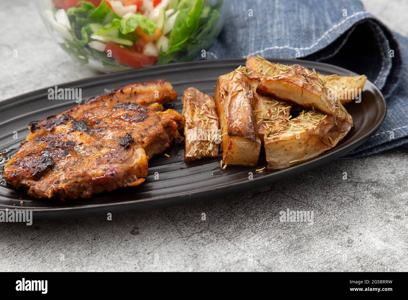 Lammkotelett auf einem schwarzen Gericht mit mit Rosmarin überzogenen Kartoffelkeilen und Salat Stockfoto
