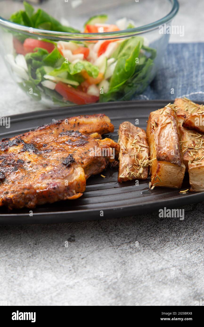 Lammkotelett auf einem schwarzen Gericht mit mit Rosmarin überzogenen Kartoffelkeilen und Salat Stockfoto