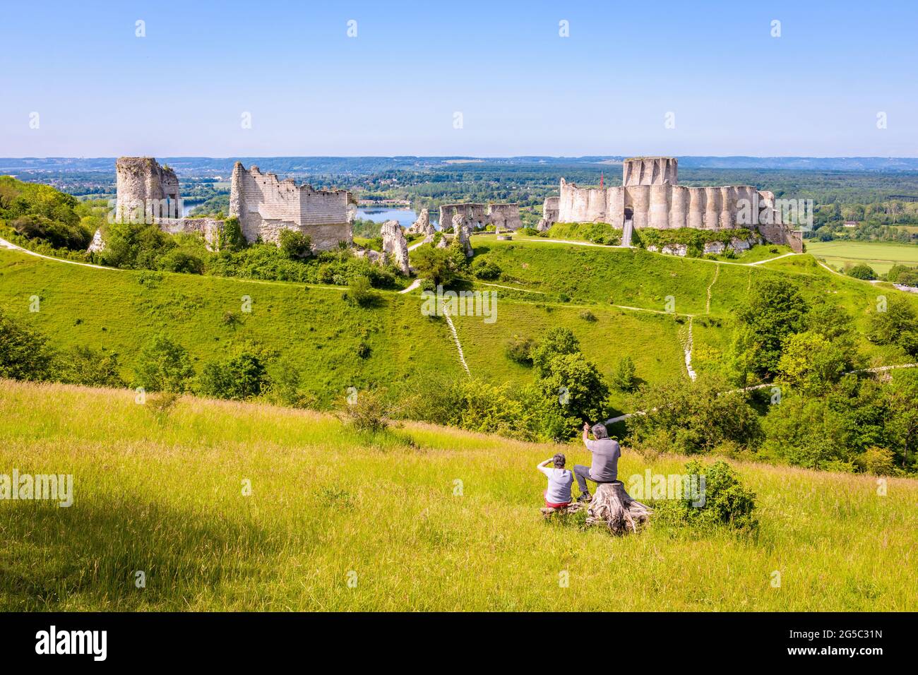 Ein Seniorenpaar sitzt auf einem Stumpf und beobachtet die Ruinen von Château-Gaillard, einer befestigten Burg, die Richard Löwenherz in der Normandie errichtet hat. Stockfoto