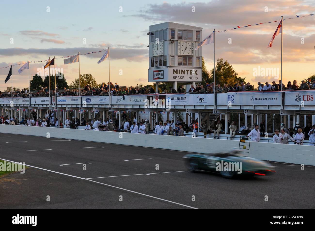 Historische Autorennen bis in den Abend mit einem Oldtimer-Rennen beim Goodwood Revival 2012, das bei Sonnenuntergang durch das Boxenviertel führt. Ausdauer wird wiederhergestellt Stockfoto