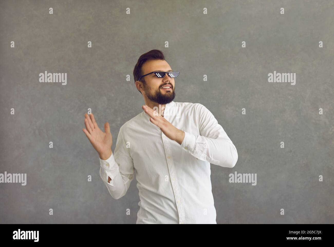 Fröhlicher junger Mann in einer zermollten Lebensbrille, der auf grauem Hintergrund zu Musik tanzt Stockfoto