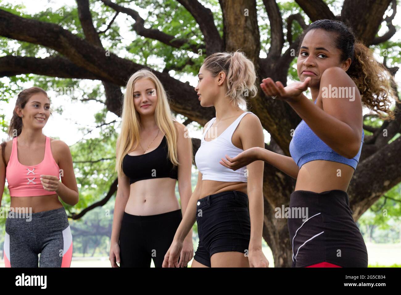 Schwarze afroamerikanische Frau fühlt sich langweilig, wenn sie am Wochenende morgens mit jungen multiethnischen Frauen in der Gruppe von Freunden im Yoga-Übungskurs im Park spricht. Stockfoto