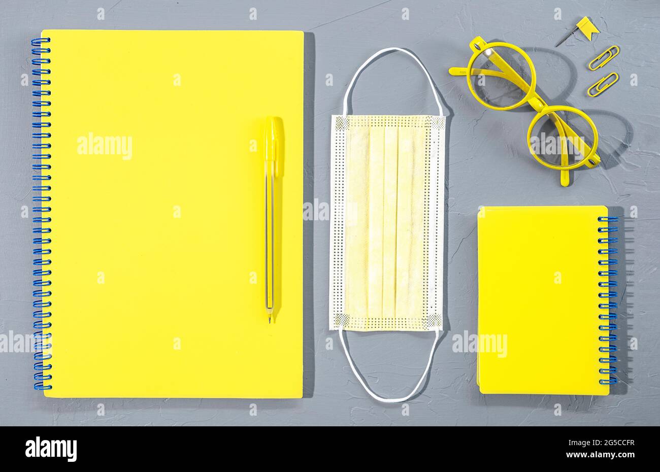 Verschiedene gelbe Büro- und Schulbedarf Bürobedarf mit Brille und medizinischer Maske auf grauem Hintergrund. Stockfoto
