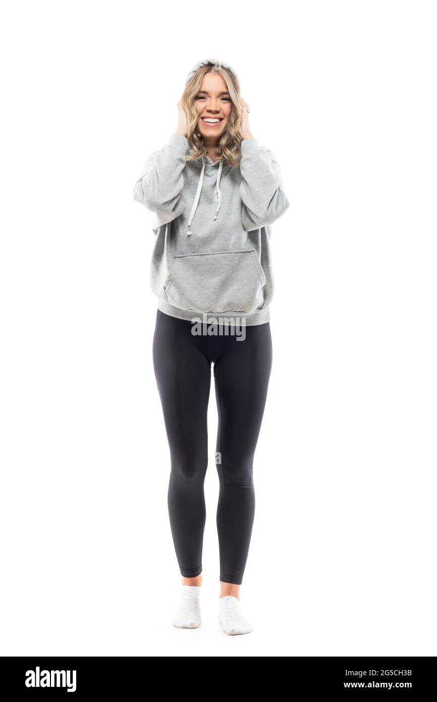 Fröhliche, aufgeregte junge Frau in sportlich-lässigen Leggings und grauem Kapuzenpullover. Ganzkörperlänge isoliert auf weißem Hintergrund. Stockfoto