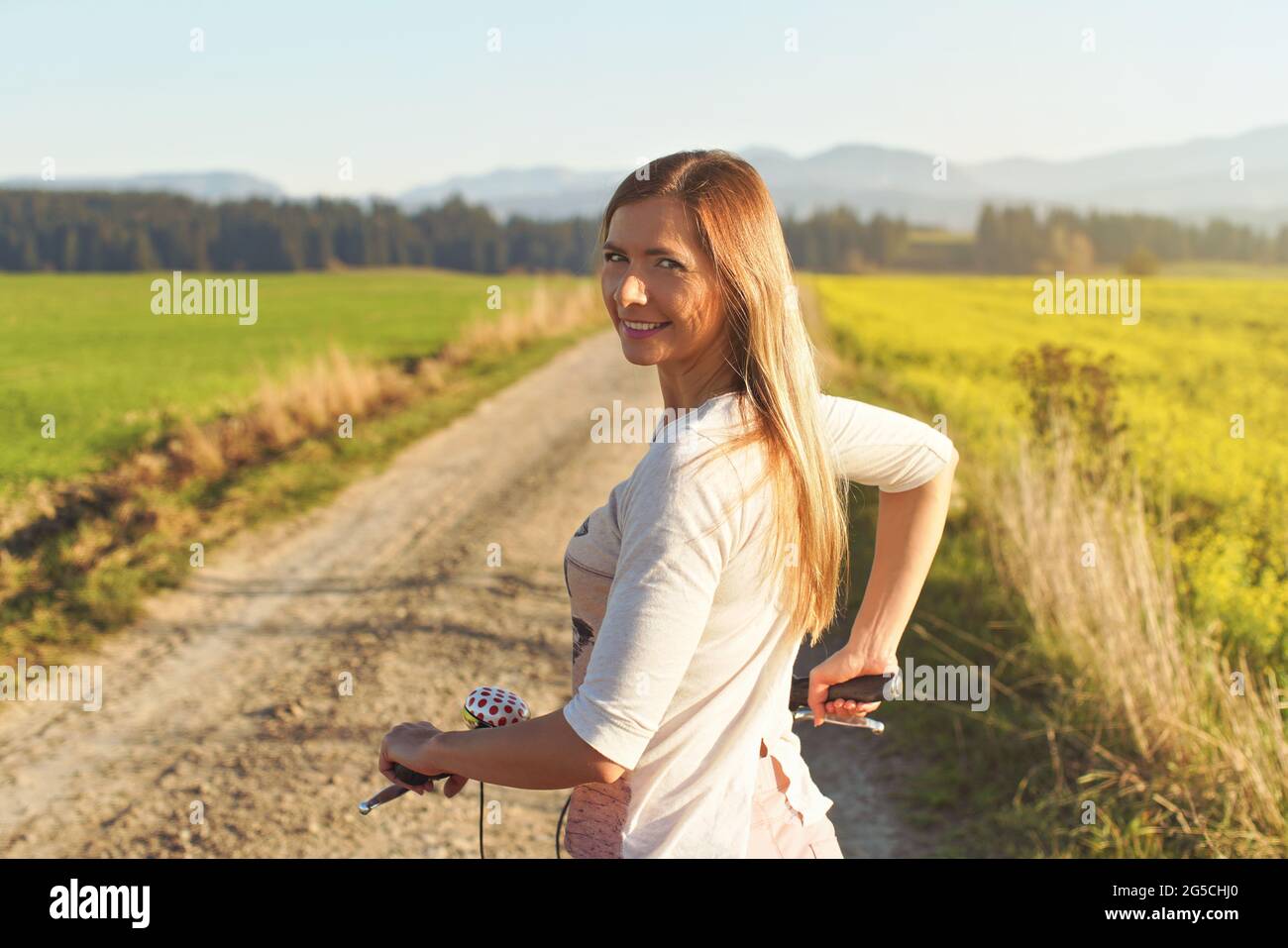 Junge Frau, die neben ihrem Fahrrad auf einer staubigen Landstraße steht und über die Schulter zurückblickt Stockfoto