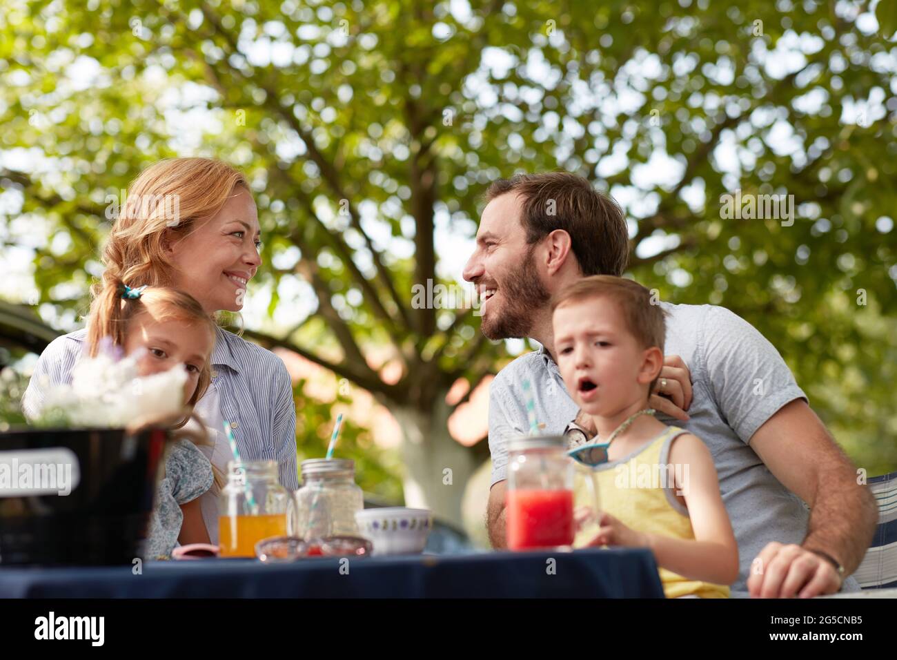 Mutter und Vater mit ihren Kindern in Runden sitzen draußen in der Natur, schauen sich gegenseitig an und lächeln Stockfoto