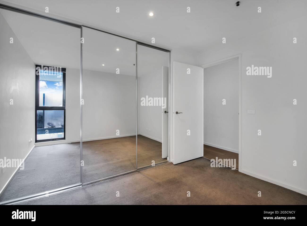 Leeres Schlafzimmer mit weißen Wänden und einem Kleiderschrank mit Spiegeltüren Stockfoto