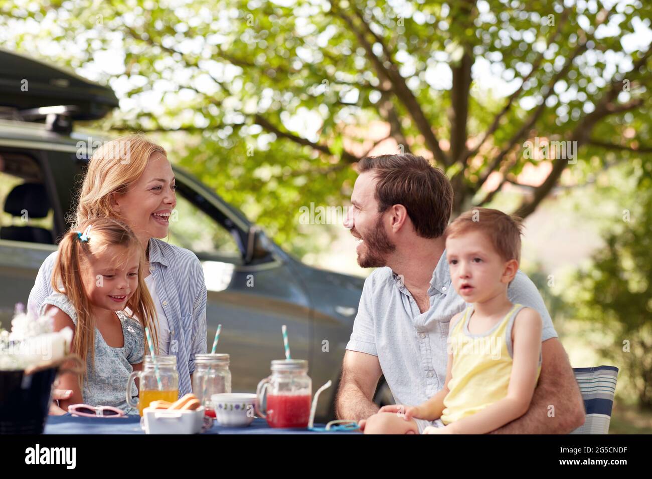 Fröhliche kaukasische Eltern schauen sich gegenseitig, lächeln, lachen, mit ihren Kindern im Schoß Stockfoto