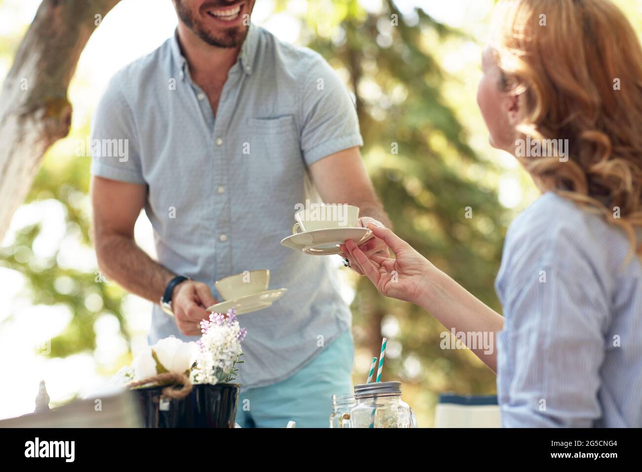 Beschnittenes Bild eines bärtigen Mannes, der seiner Frau mit einem Lächeln eine Tasse Kaffee gab Stockfoto