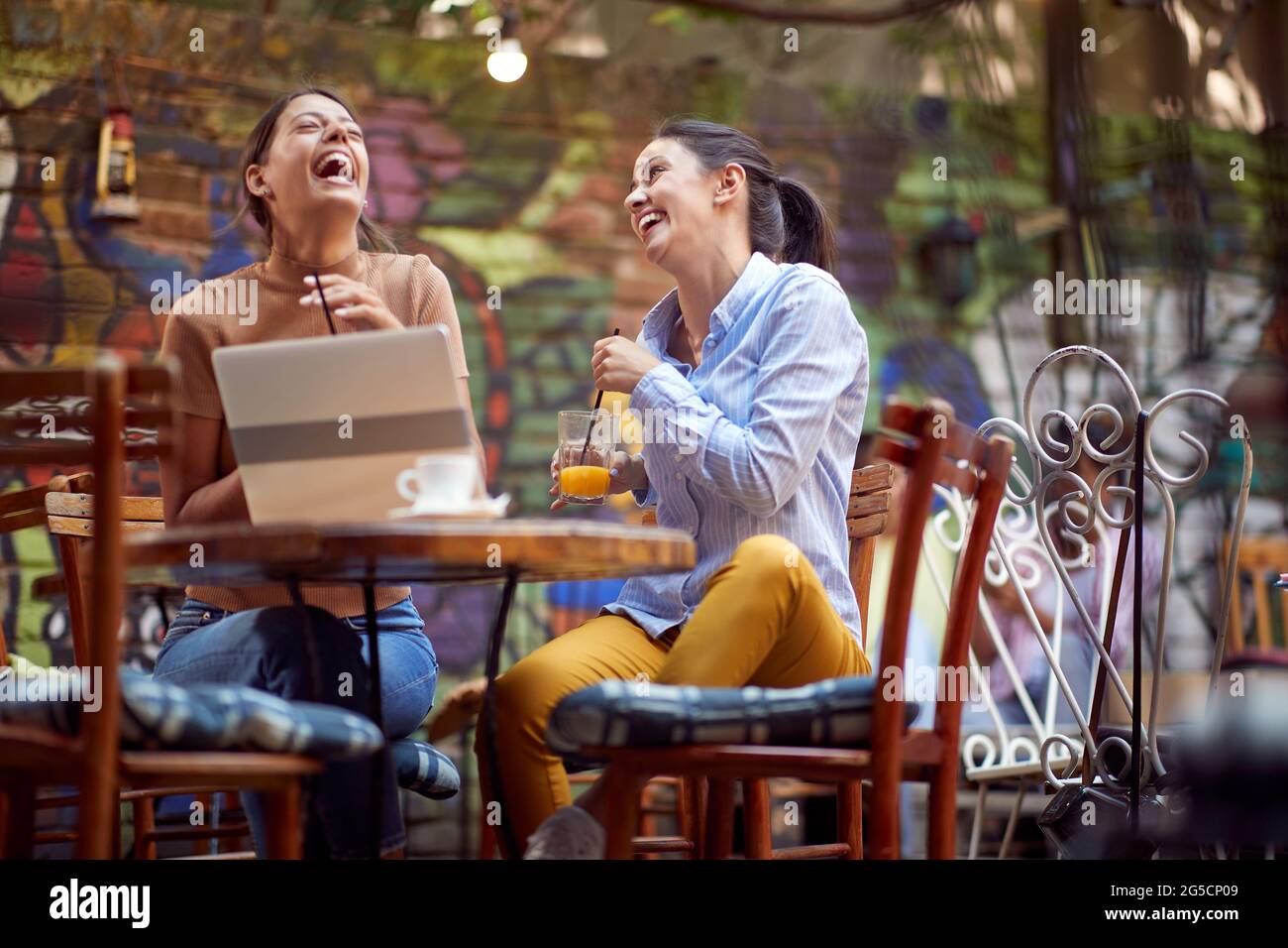 Zwei wunderschöne kaukasische junge Erwachsene Freundinnen, die im Café mit offener Tür sitzen und laut lachen. Stockfoto