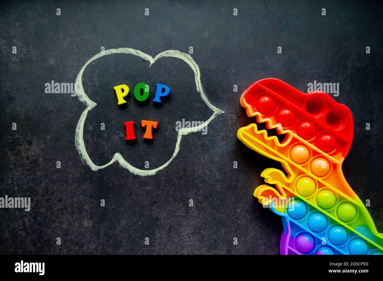 Pop it Dinosaurier Spielzeug Regenbogenfarben auf schwarzem Hintergrund mit bunten Buchstaben und der Inschrift - Pop it in einer Sprechblase. Stockfoto