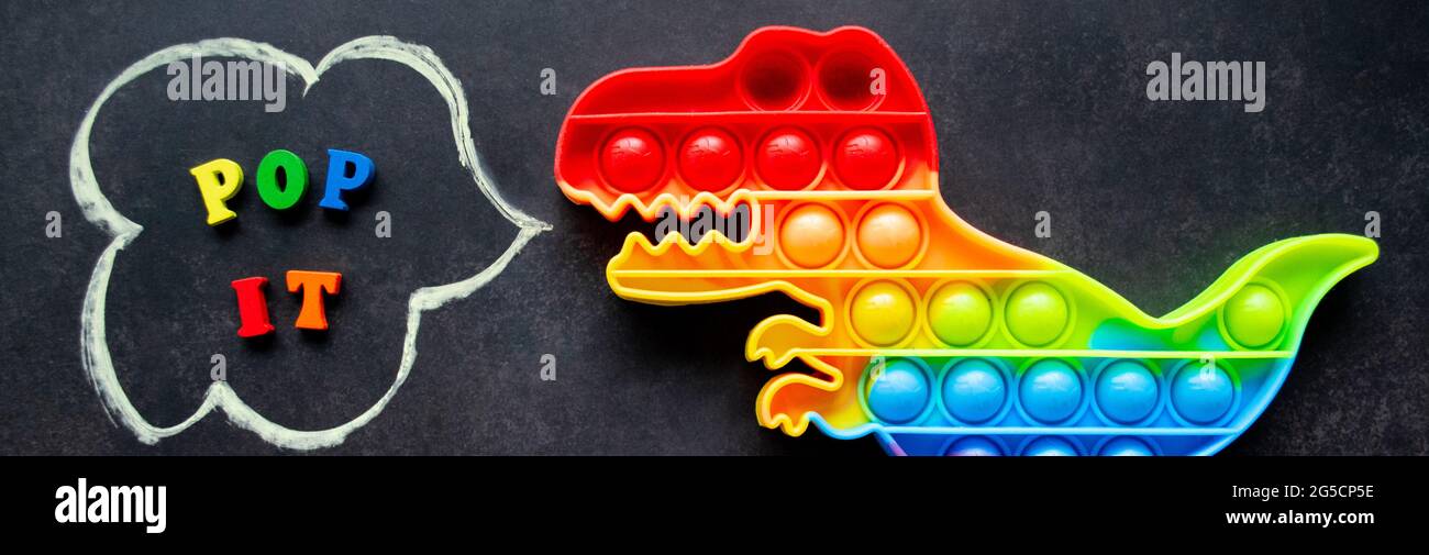 Banner mit Pop IT Dinosaurier Spielzeug Regenbogenfarben auf schwarzem Hintergrund mit bunten Buchstaben und der Inschrift - Pop it in einer Sprechblase. Stockfoto