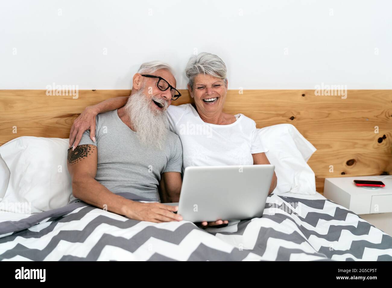Glückliches Seniorenpaar, das Spaß daran hat, einen Laptop im Bett zu sehen - Technik und Lifestyle-Konzept für ältere Menschen Stockfoto