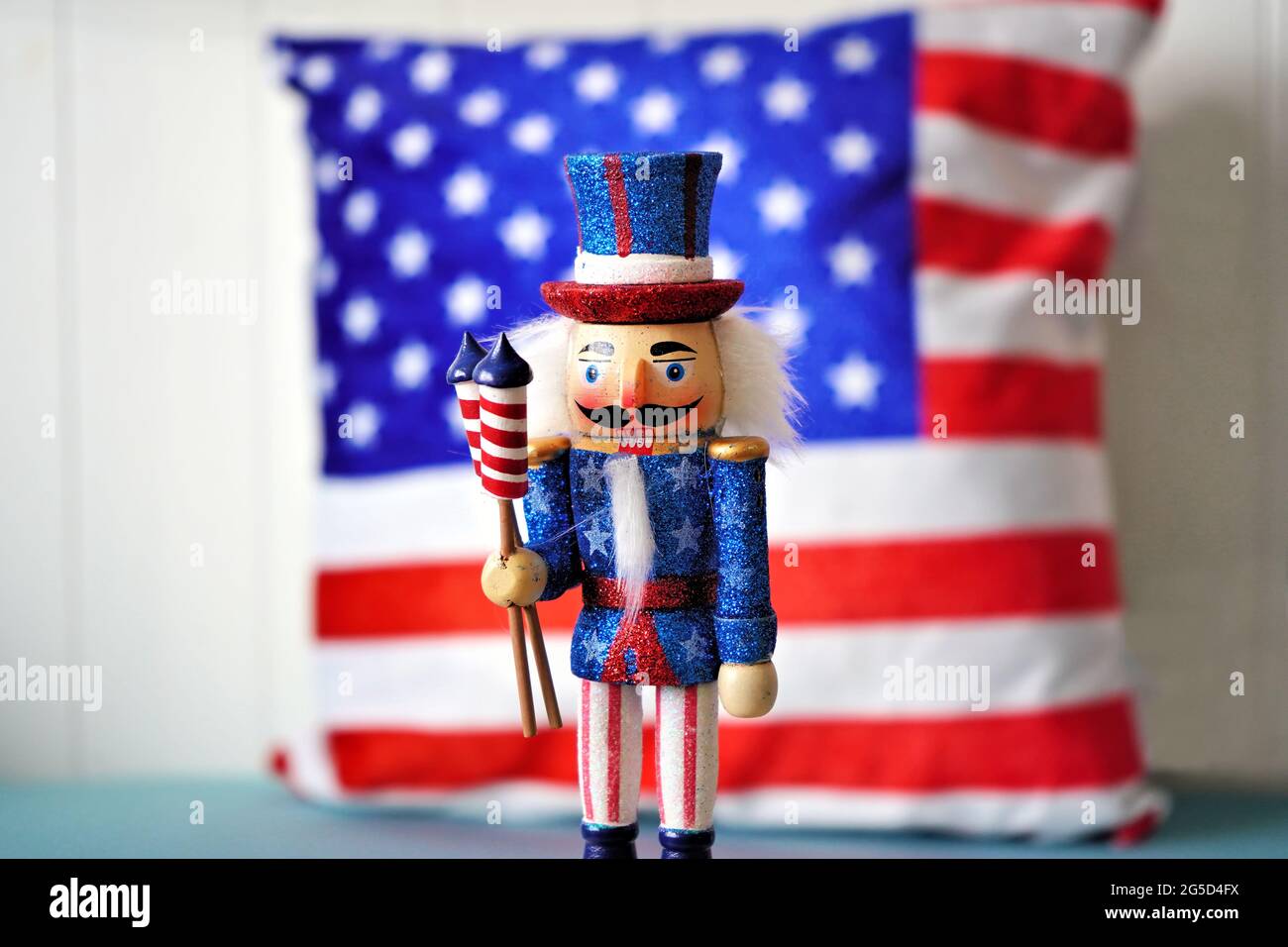 4. Juli Zimmerdekoration: Ein amerikanischer Nussknacker, der die US-Flagge vor einem Kissen in den gleichen Farben hält. Stockfoto