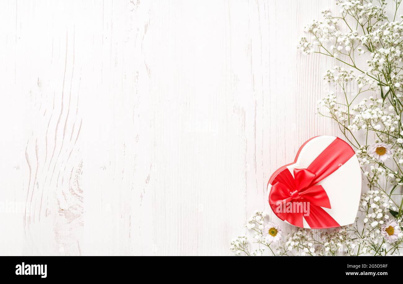 Blumen Komposition mit Geschenk und leerem Platz für Ihren Text. Weiße Blumen auf weißem Holzhintergrund und geformtes Herzgeschenk. Hochzeit mockup mit klein Stockfoto