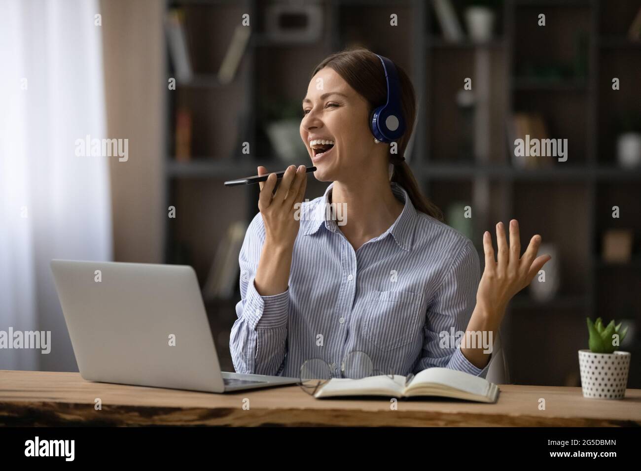 Fröhliche, emotionale junge Frau, die Song in der mobilen App aufzeichnet. Stockfoto