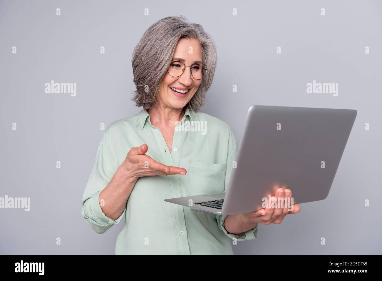 Porträt von attraktiven trendigen fröhlich grauhaarige Frau mit Laptop Surfen Web Lachen isoliert über grauen Pastellfarben Hintergrund Stockfoto