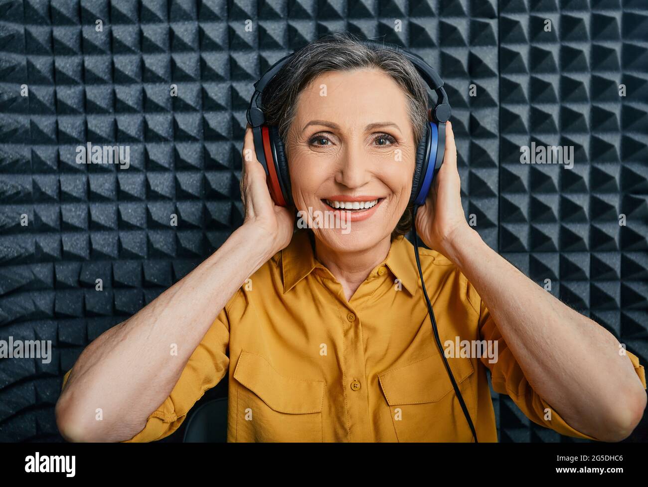 Behandlung von Hörverlust. Positive reife Frau mit Audiometrie-Kopfhörern beim Hörtest und Audiogramm in einem speziellen Audioraum Stockfoto