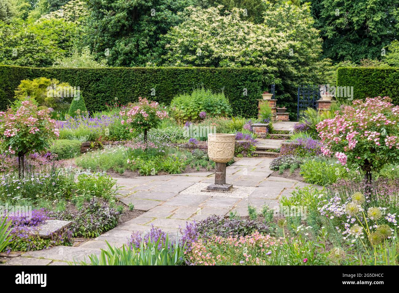 Friedliche Ecke eines gefackelten englischen formalen Gartens mit Steinvase. Stockfoto