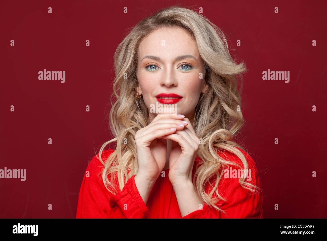 Lächelnde Frau mit blondem Haar und natürlich gepflegten Nägeln auf lebhaft rotem Hintergrund Stockfoto