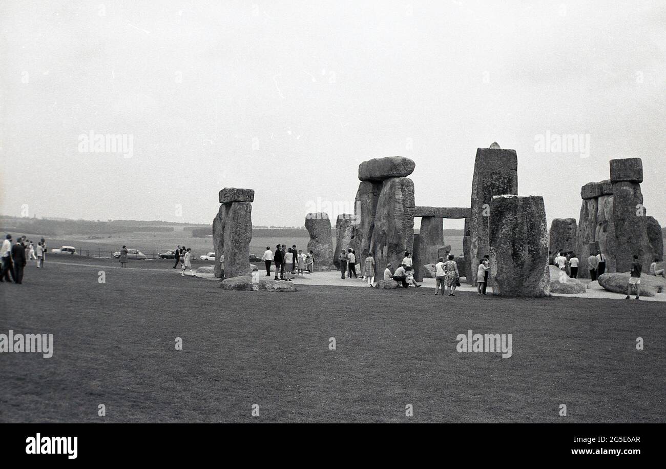 1960er Jahre, historische, Außenansicht der Besucher an den alten Steinen in Stonehenge, Wiltshire, England, UK. Zu dieser Zeit konnte man frei um die prähistorischen Steine gehen, Aber in den folgenden zehn Jahren wurden aufgrund der Besucherzahlen, der Beschädigung des Grases und der Erosion an der heiligen, alten Grabstätte die Steine abgetragen, um den Zugang zu verhindern. Sir Cecil Chubb, der sich auf dem Anwesen der Abtei von Amesbury befindet, das sich zu einer Zeit im Besitz von König Heinrich VIII. Befindet, brachte das Grundstück mit den Steinen auf einer Auktion im Jahr 1915 und gab es 1918 an die britische Nation. Stockfoto