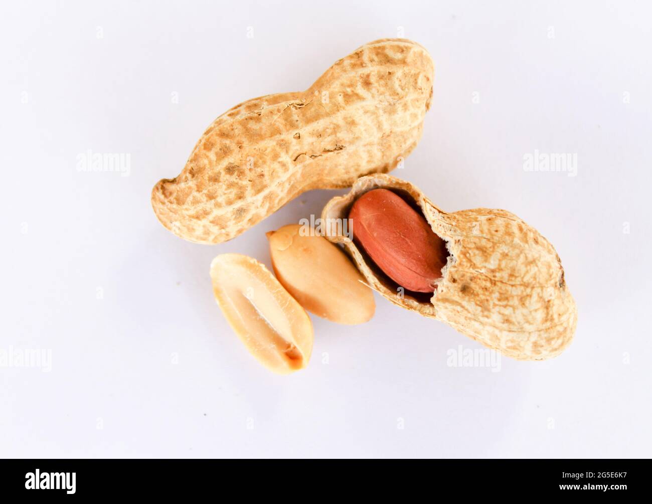 Draufsicht auf Erdnüsse auf weißem Hintergrund. Erdnüsse werden geschält, um rote Samen im Inneren zu offenbaren. Es gab einen Samen, der auf der Seite entfernt worden war. Stockfoto