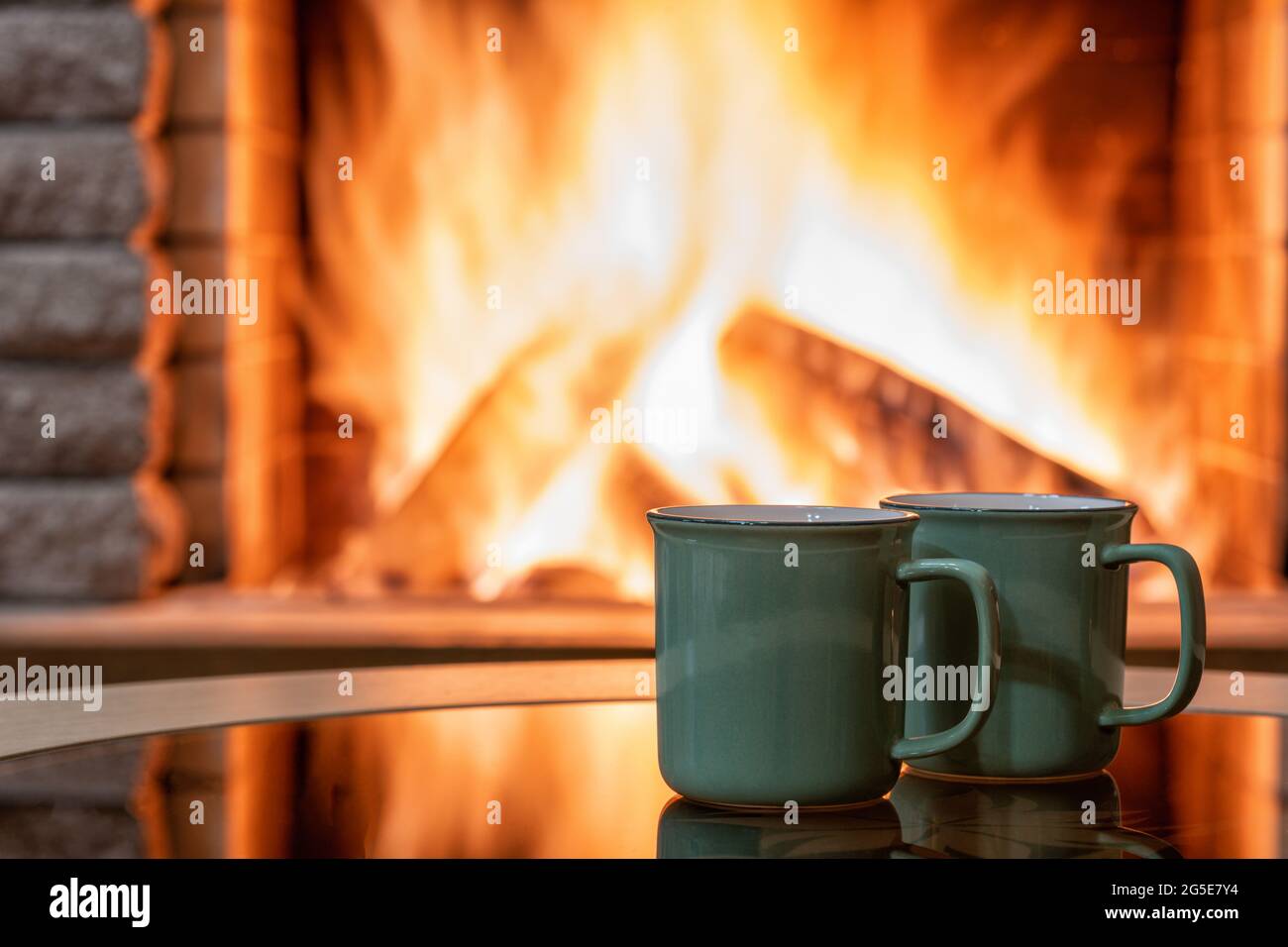 Gemütlicher Kamin und Teebecher, Reflexion von einem Feuer auf einem Glastisch. Stockfoto