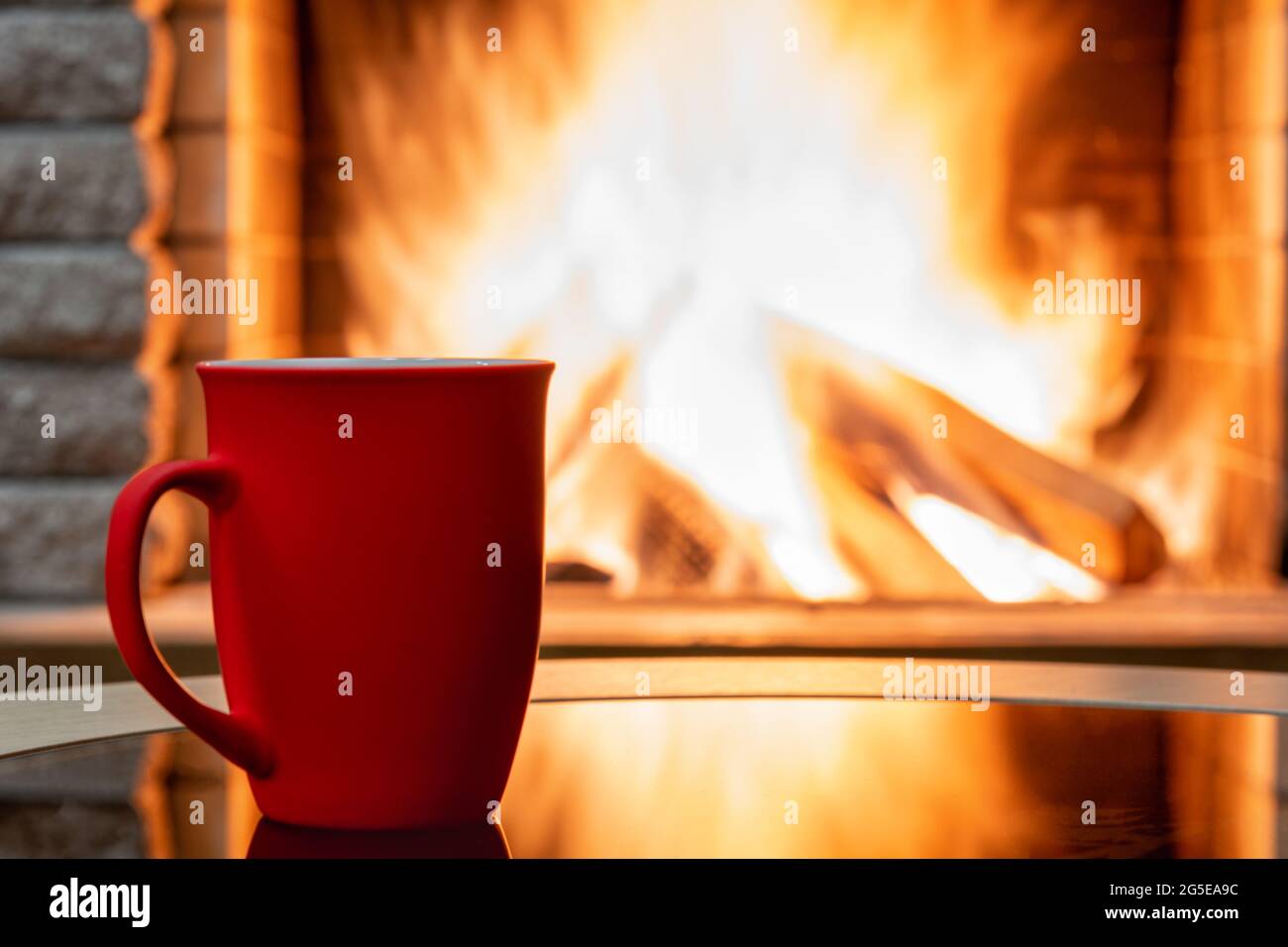 Gemütliche Kamin-Szene und große Tasse Tee, Reflexion von einem Feuer auf einem Glastisch. Stockfoto