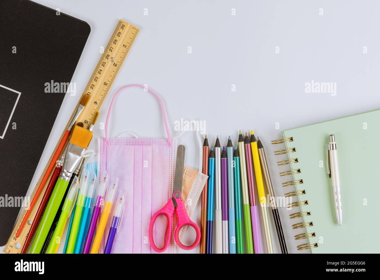Schule liefert Buntstifte auf einer sicheren Coronavirus COVID-19 Pandemie medizinischen hygienischen Masken Stockfoto