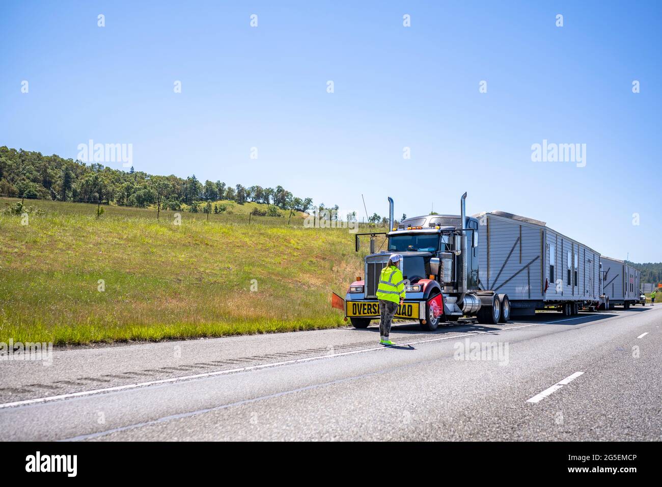 Speziell ausgestattete große Rig-Sattelschlepper, die übergroße Manufakturhäuser auf Step-Down-Sattelaufliegern transportieren, bereiten sich darauf vor, die Autobahn zu betreten Stockfoto