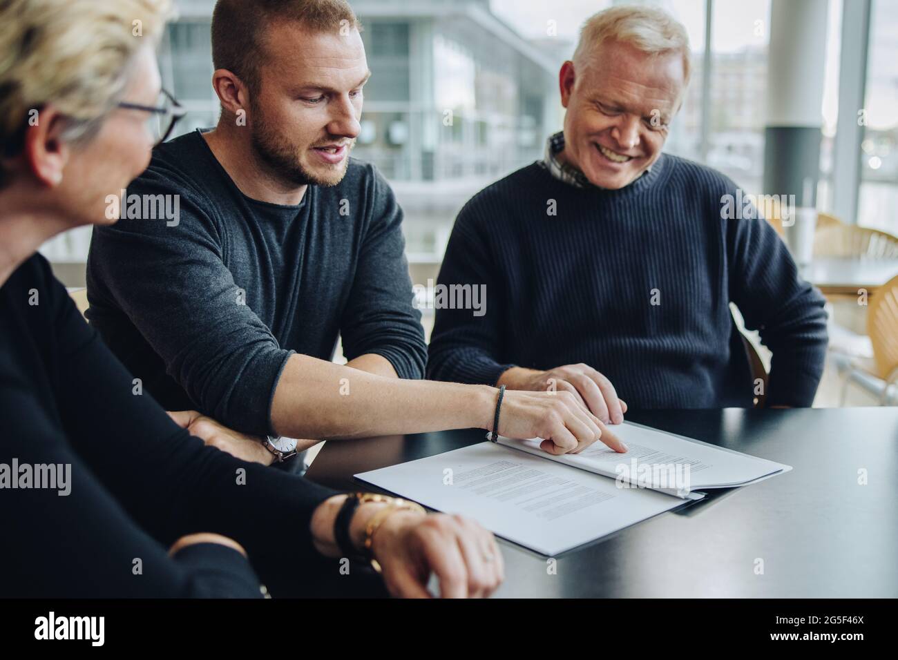 Junger Geschäftsmann, der während des Treffens das Einverständnisdokument liest. Geschäftsteam diskutiert die Bedingungen im Vertragsdokument. Stockfoto