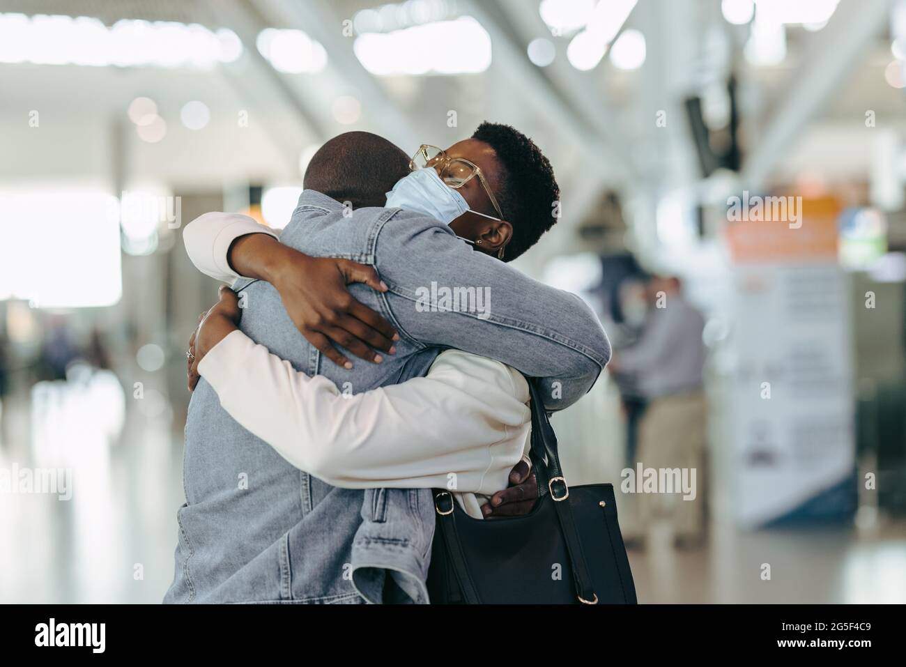 Afrikanisches Reisepaar während eines Pandemietreffens am Flughafen. Mann am Flughafenterminal umarmt Frau mit Gesichtsmaske vor dem Abflug. Stockfoto