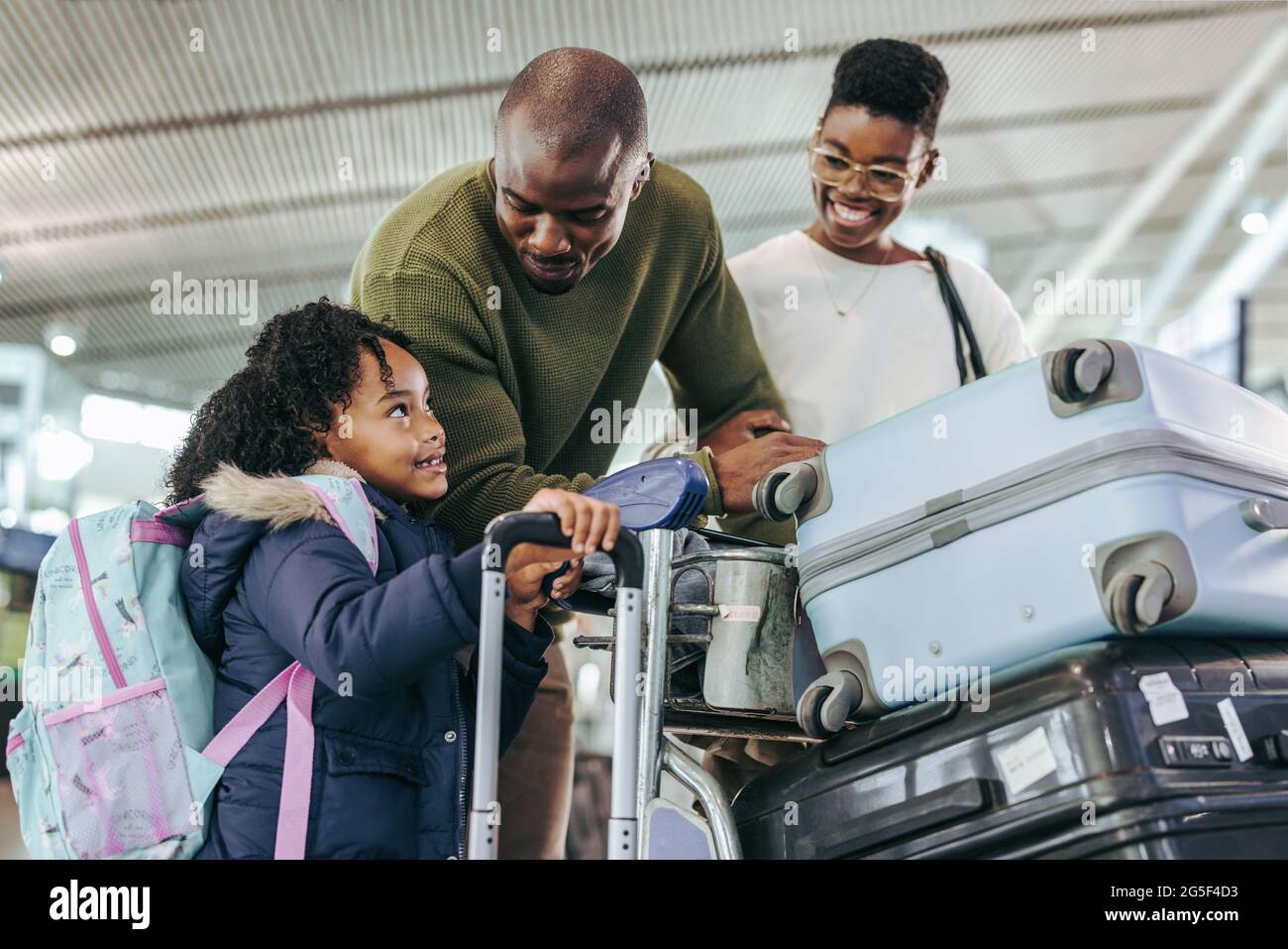 Ein Touristenpaar schaute seine Tochter an, während es mit Gepäck am Flughafen stand. Afrikanisches Kind im Gespräch mit ihren Eltern am Flughafenterminal. Stockfoto