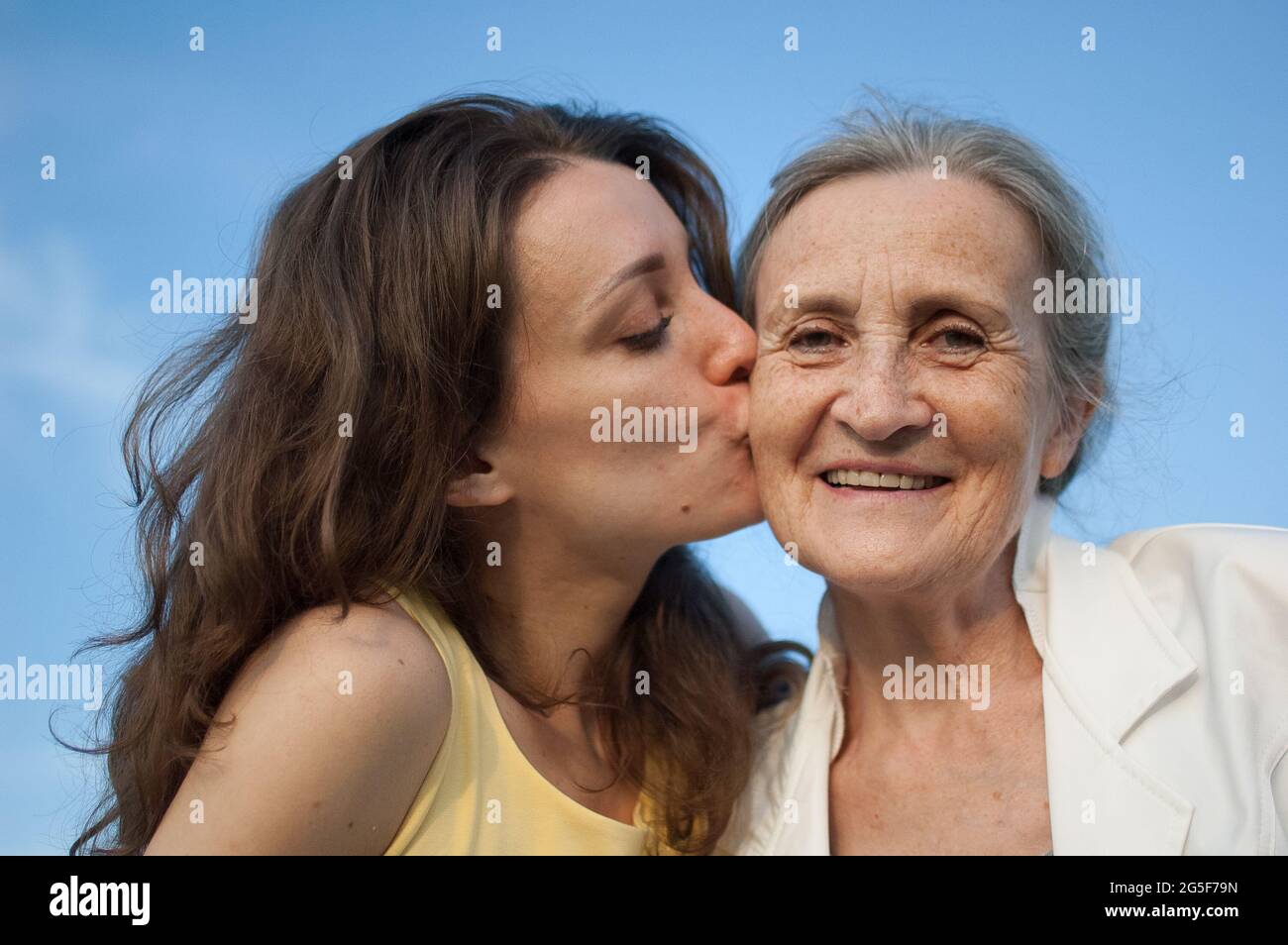 Ältere Mutter mit grauen Haaren und ihrer erwachsenen Tochter suchen An der Kamera im Garten und umarmt sich gegenseitig An sonnigen Tagen im Freien Stockfoto