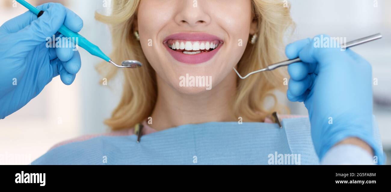 Eine weibliche Patientin, die ihre weißen Zähne zeigte, während sie in der Zahnklinik untersucht wurde, Zahnarzthände in Gummihandschuhen, die Zahnwerkzeuge hielten, Panorama Stockfoto