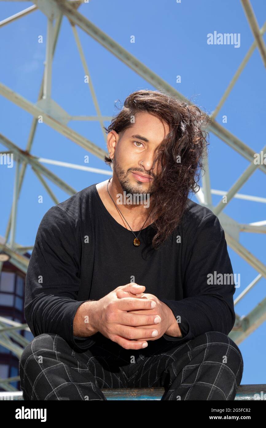 Porträt eines jungen Mannes, der in einem Skatepark sitzt und eine akrobatische Straßentänzerin mit langen Haaren ist. Stockfoto