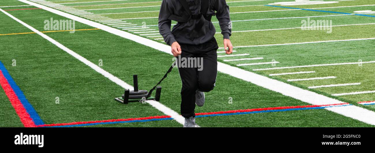 Vorderansicht eines Athleten, der einen Schlitten mit Gewicht auf einem grünen Rasenfeld zieht und dabei Schweißausbrüche trägt. Stockfoto