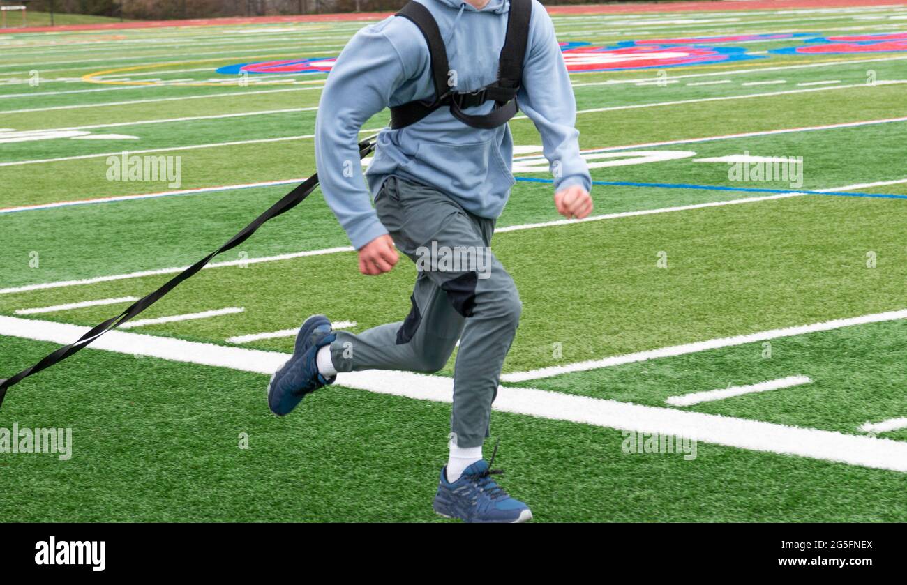 Nahaufnahme eines Läufers, der einen Schlitten mit Gewichten auf einem grünen Rasen zieht, während der High School-Trainingsstrecke. Stockfoto