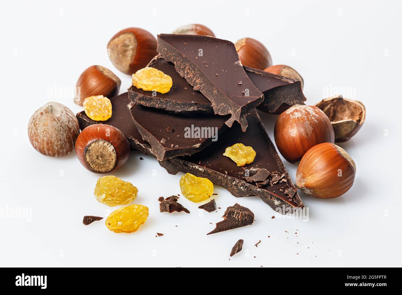Nüsse, süße Rosinen und und Stapel einer dunklen Schokolade auf weißem Hintergrund. Reife wilde Haselnüsse und bittere Schokolade. Natürliche Bio-Produkte. Kopieren Stockfoto