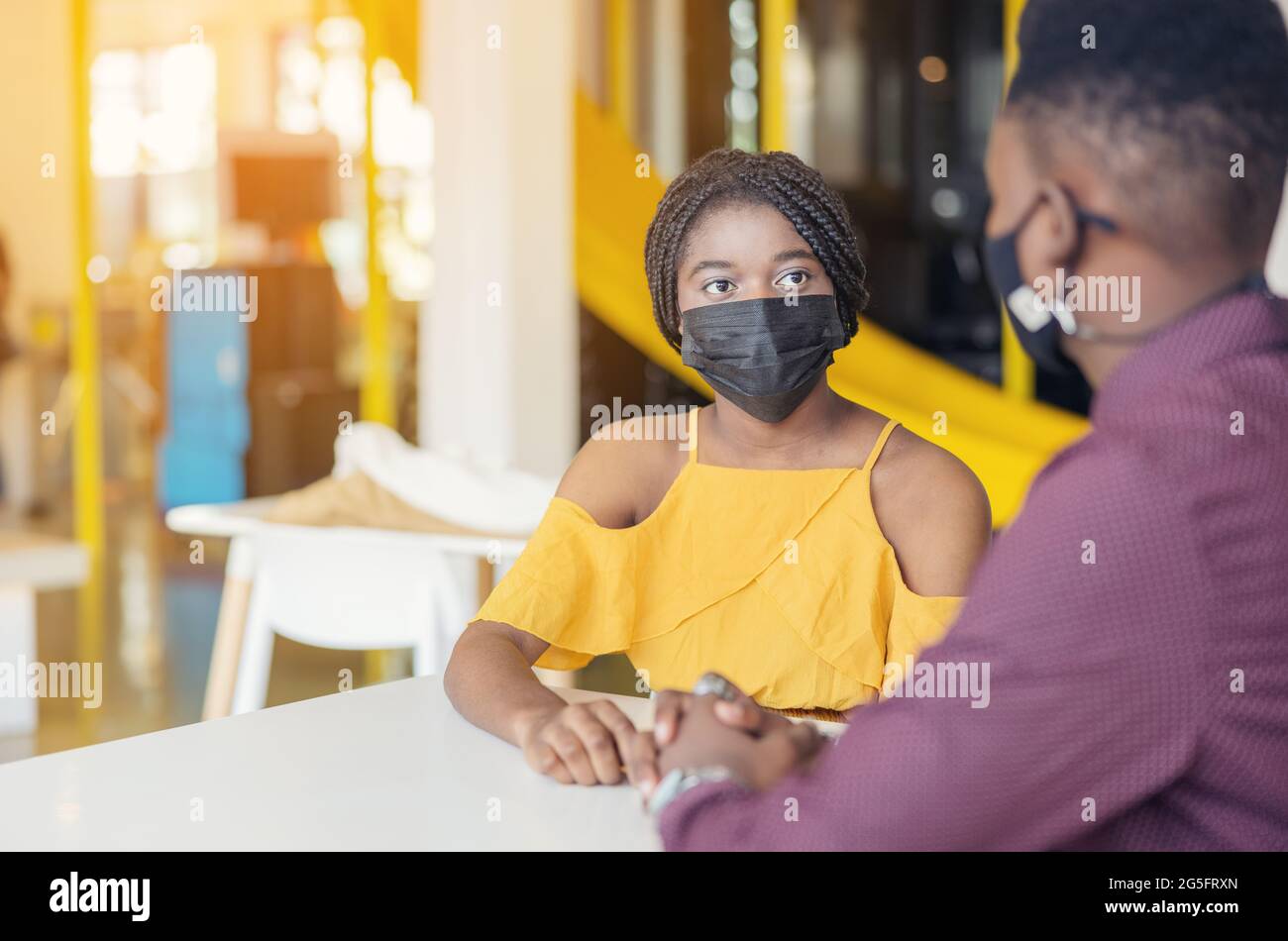 Afrikanische Studenten mit Freunden, die eine Maske tragen, sitzen am Schreibtisch der modernen Schule. Virenschutz In Der Schule. Selektiver Fokus Stockfoto